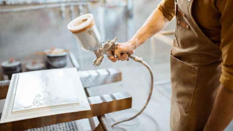 woodworker spraying paint on a  finished wood item